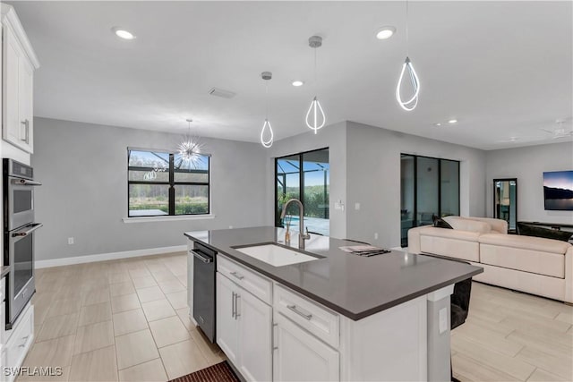 kitchen with an island with sink, white cabinets, sink, and pendant lighting