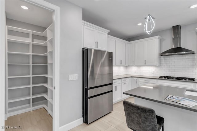 kitchen with white cabinetry, appliances with stainless steel finishes, tasteful backsplash, wall chimney range hood, and pendant lighting