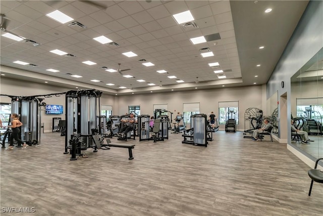 exercise room with a paneled ceiling, light hardwood / wood-style floors, and a towering ceiling