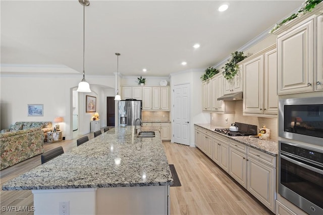 kitchen featuring appliances with stainless steel finishes, an island with sink, hanging light fixtures, and backsplash