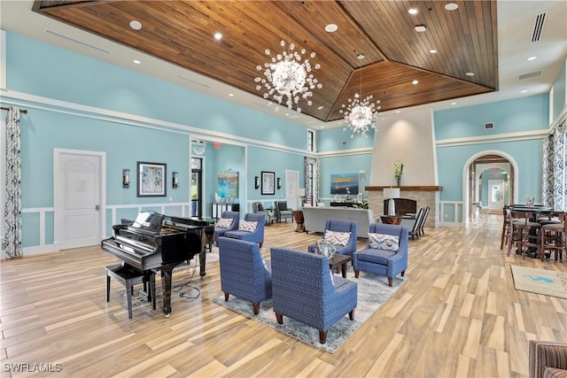 living room with a chandelier, wooden ceiling, a tray ceiling, light hardwood / wood-style floors, and a high ceiling