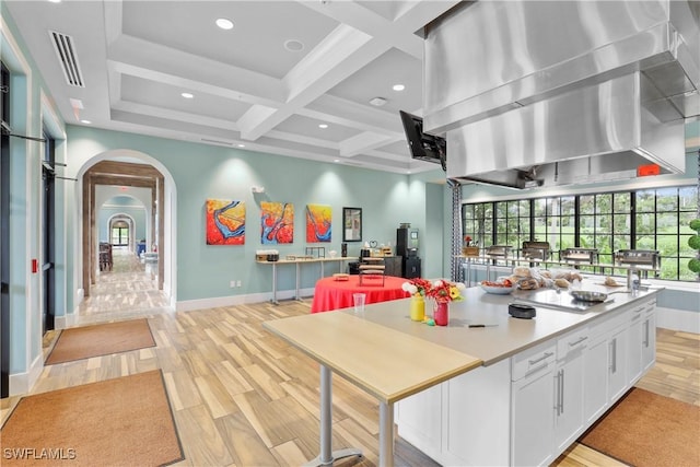 kitchen with coffered ceiling, white cabinetry, light hardwood / wood-style flooring, island exhaust hood, and beam ceiling