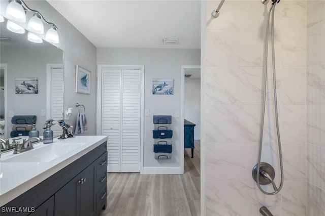 bathroom featuring hardwood / wood-style flooring, a tile shower, and vanity