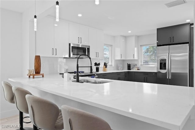 kitchen with kitchen peninsula, stainless steel appliances, hanging light fixtures, white cabinets, and a breakfast bar