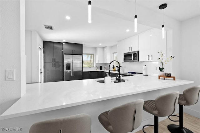 kitchen with kitchen peninsula, appliances with stainless steel finishes, hanging light fixtures, white cabinets, and sink