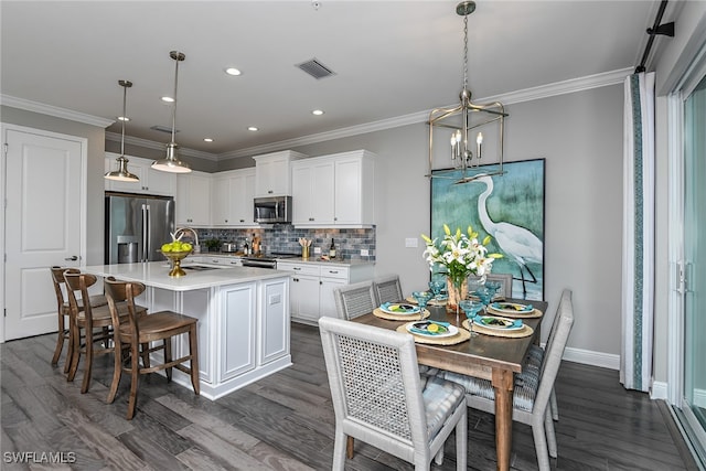 kitchen featuring appliances with stainless steel finishes, a kitchen island with sink, dark wood-type flooring, decorative light fixtures, and white cabinetry