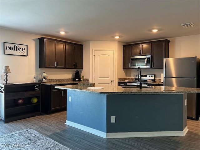 kitchen with stainless steel appliances, a center island with sink, dark brown cabinetry, and hardwood / wood-style floors