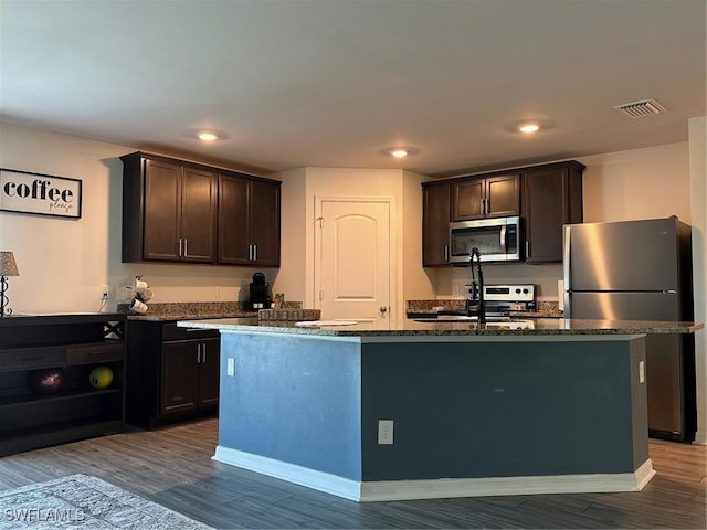 kitchen featuring appliances with stainless steel finishes, an island with sink, hardwood / wood-style floors, and dark brown cabinets