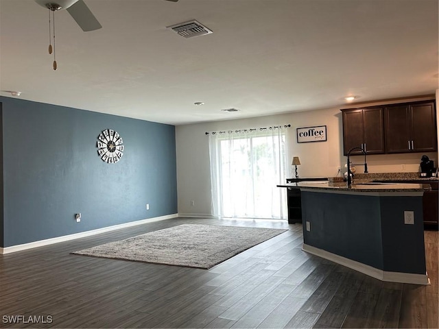 kitchen with dark wood-type flooring, an island with sink, dark brown cabinetry, ceiling fan, and sink