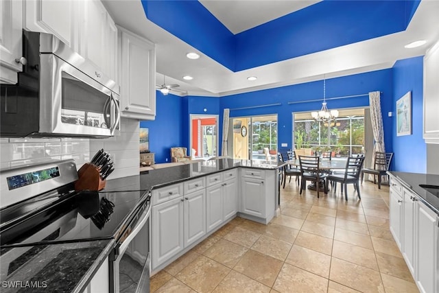 kitchen featuring kitchen peninsula, decorative backsplash, hanging light fixtures, stainless steel appliances, and white cabinets