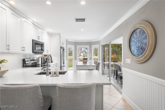 kitchen with stainless steel appliances, white cabinetry, a kitchen breakfast bar, light tile patterned floors, and kitchen peninsula