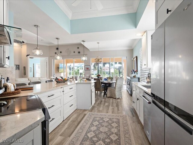 kitchen with light stone counters, decorative light fixtures, light hardwood / wood-style floors, white cabinets, and appliances with stainless steel finishes