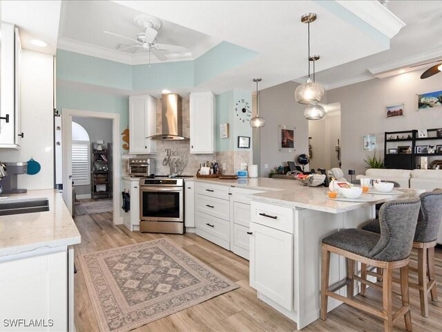 kitchen featuring wall chimney range hood, stainless steel stove, white cabinetry, and hanging light fixtures