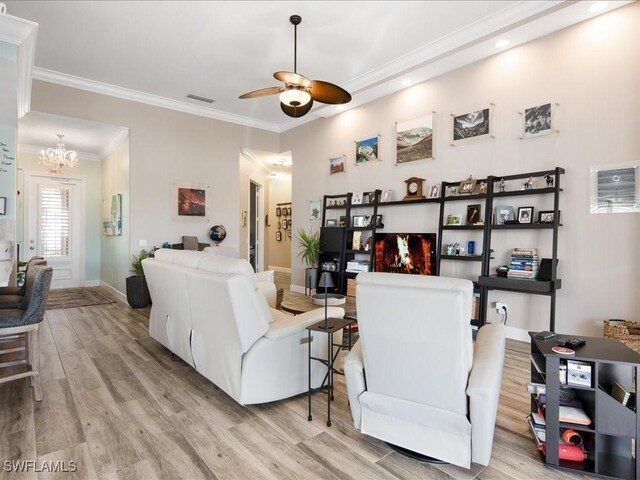 living room with ceiling fan with notable chandelier, light wood-type flooring, and ornamental molding