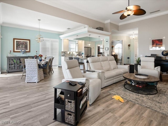 living room with ceiling fan with notable chandelier, light wood-type flooring, and crown molding