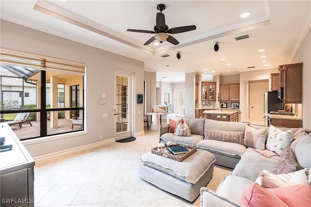 living room featuring ceiling fan, ornamental molding, a raised ceiling, and sink