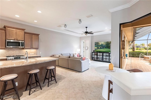 kitchen featuring decorative backsplash, ornamental molding, ceiling fan, light stone counters, and a breakfast bar area