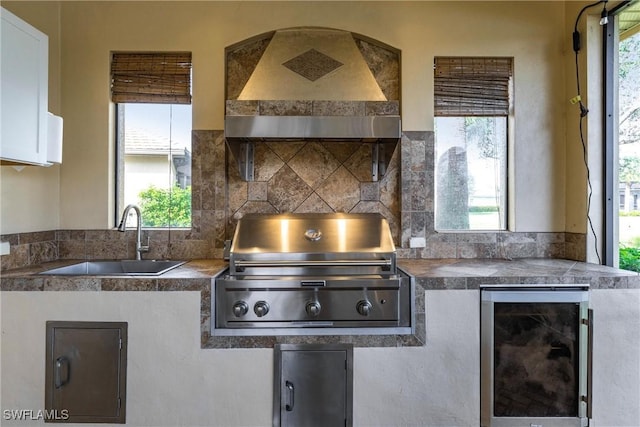 kitchen with wine cooler, custom exhaust hood, sink, white cabinetry, and plenty of natural light