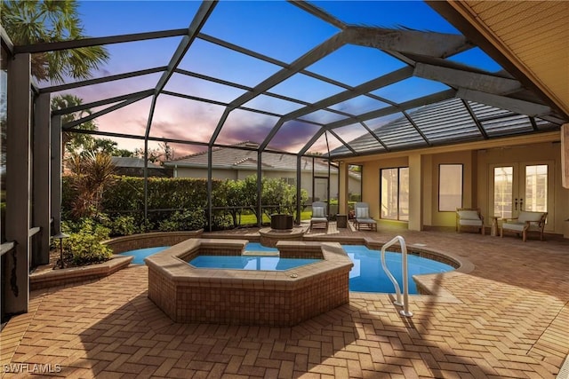 pool at dusk featuring a lanai, an in ground hot tub, french doors, and a patio