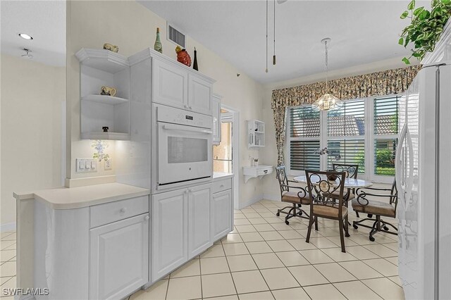 kitchen with light tile patterned floors, white appliances, white cabinetry, and pendant lighting