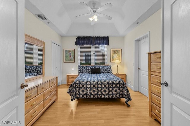 bedroom featuring a raised ceiling, ceiling fan, light hardwood / wood-style flooring, and multiple windows