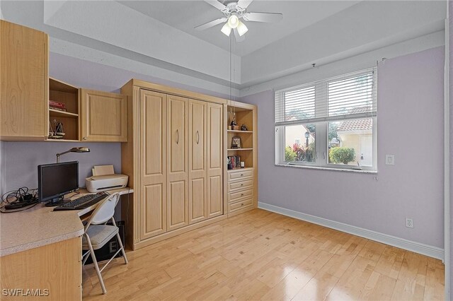 office space featuring a raised ceiling, ceiling fan, and light hardwood / wood-style floors