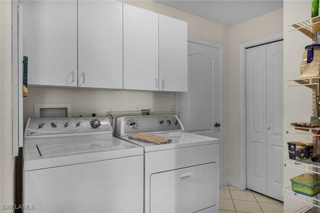 laundry room featuring washing machine and dryer, light tile patterned flooring, and cabinets