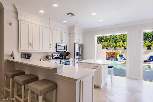 kitchen with a breakfast bar area, appliances with stainless steel finishes, ornamental molding, white cabinets, and kitchen peninsula