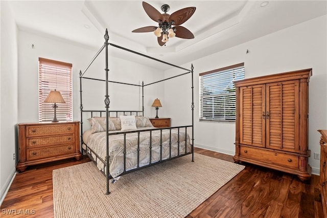 bedroom with ceiling fan, dark hardwood / wood-style flooring, and a tray ceiling