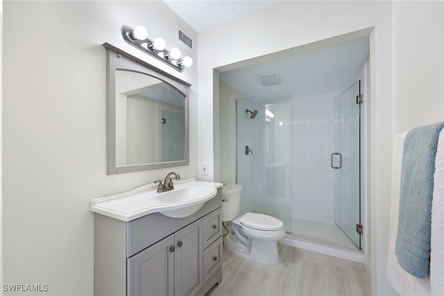 bathroom with wood-type flooring, vanity, toilet, and a shower with shower door