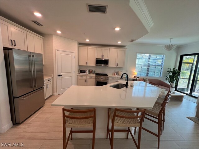 kitchen with white cabinetry, a center island with sink, appliances with stainless steel finishes, ornamental molding, and sink