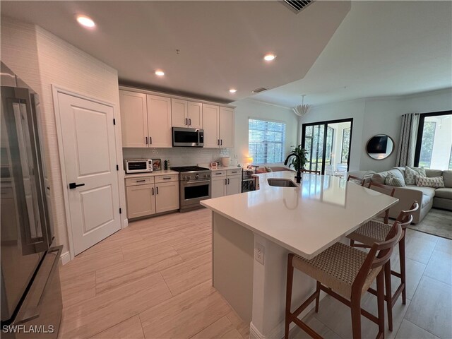 kitchen with a kitchen bar, white cabinetry, stainless steel appliances, sink, and a center island with sink