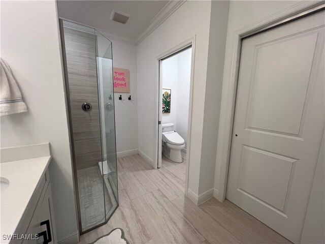 bathroom with toilet, vanity, hardwood / wood-style floors, ornamental molding, and a tile shower