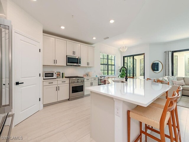 kitchen with white cabinets, a kitchen bar, appliances with stainless steel finishes, and a center island with sink