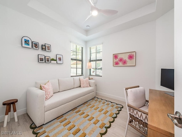 living room featuring ceiling fan, a tray ceiling, and light hardwood / wood-style floors