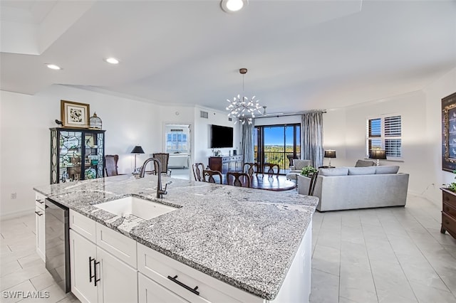 kitchen featuring dishwasher, open floor plan, a sink, a kitchen island with sink, and a notable chandelier