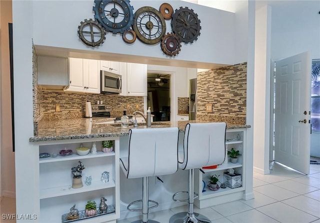 kitchen with kitchen peninsula, appliances with stainless steel finishes, tasteful backsplash, light stone counters, and white cabinetry