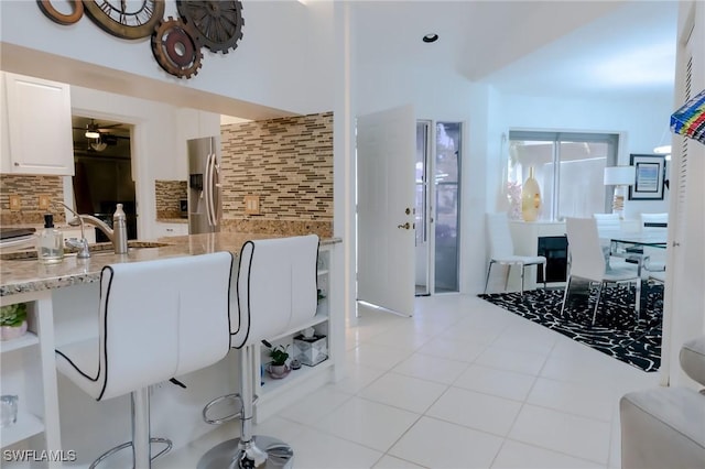 interior space featuring decorative backsplash, stainless steel fridge, sink, light tile patterned floors, and white cabinets