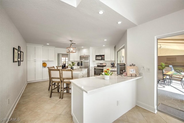 kitchen with kitchen peninsula, appliances with stainless steel finishes, hanging light fixtures, and white cabinetry