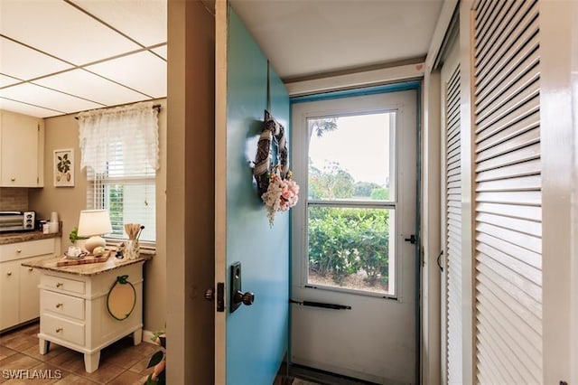 doorway with a drop ceiling and light tile patterned floors