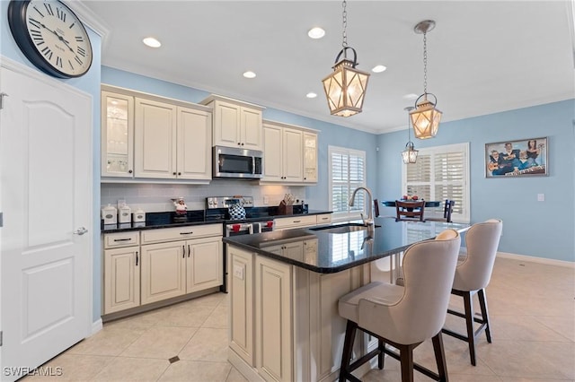 kitchen with cream cabinets, a kitchen island with sink, stainless steel appliances, a sink, and hanging light fixtures