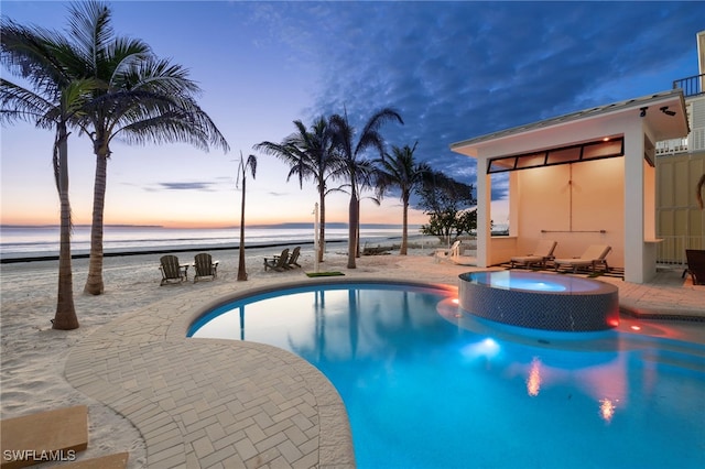 pool at dusk featuring a patio and a water view