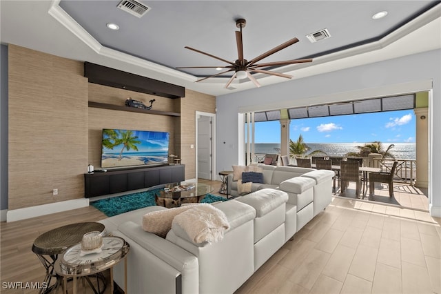 living room featuring crown molding, a tray ceiling, ceiling fan, and light wood-type flooring