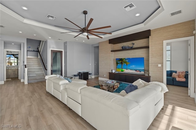 living room with a tray ceiling, ornamental molding, ceiling fan, and light wood-type flooring