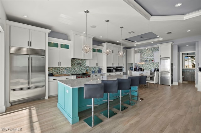 kitchen with pendant lighting, a kitchen island with sink, a kitchen breakfast bar, stainless steel built in refrigerator, and a tray ceiling