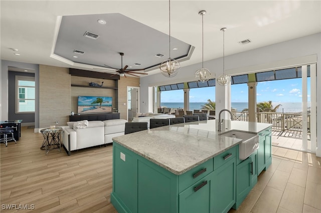 kitchen with a tray ceiling, light stone countertops, and a center island with sink