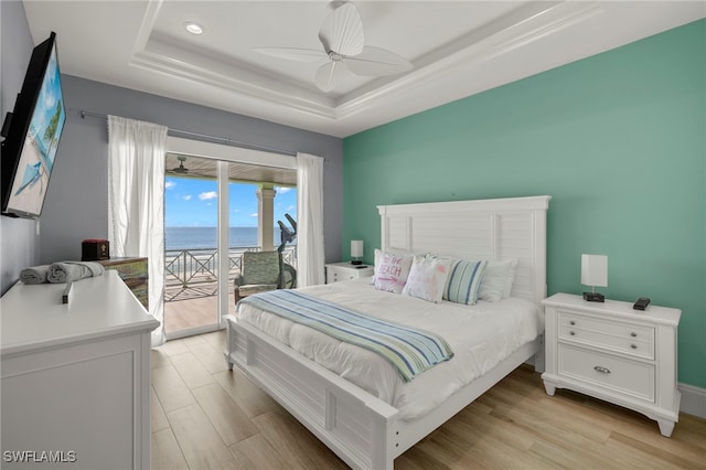 bedroom featuring a tray ceiling, access to outside, ceiling fan, light hardwood / wood-style floors, and a water view