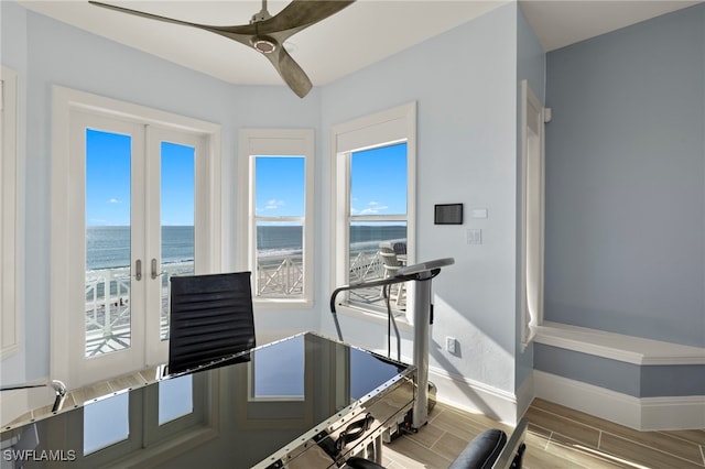 workout room featuring a water view, ceiling fan, a beach view, and french doors