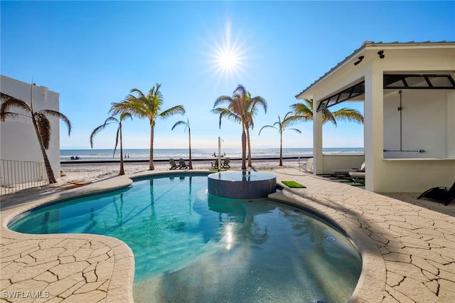 view of swimming pool featuring a water view, a beach view, and a patio area