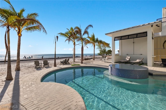 view of pool with a hot tub, a water view, and a patio area